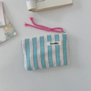 Detail of blue striped canvas pouch with pink woven zipper pull and woven brand label