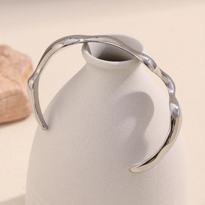 Polished silver wavy stainless steel bangle displayed on a minimalist ceramic vase