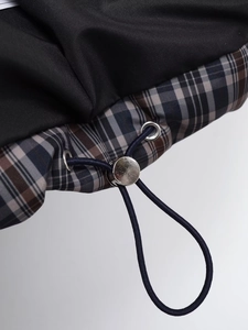 Detail of black fabric jacket with blue plaid lining, metal cord lock and drawstring