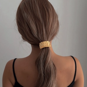Minimalist golden metal hair tie with irregular pleated texture on model's ponytail