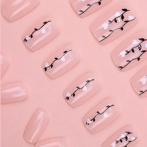 Macro detail of short square pink press-on nails with black vines and white hearts