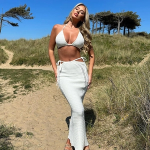 Detail of white knit halter bikini top and side cutout long skirt on a beach dune