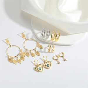 Detailed set of gold and silver heart evil eye earrings displayed on white silk fabric