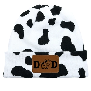 Detail of knitted cow print beanie with brown leather DAD patch and cartoon cow