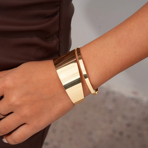 Detail of a polished gold-plated irregular wide open cuff bracelet worn on the wrist