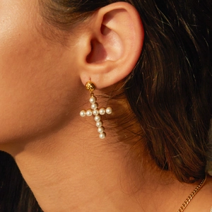 Detail showing pearl cross earring with gold metal texture and vintage design on model