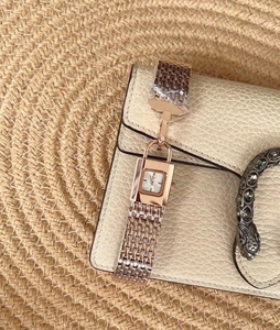 Detail of rose gold square watch with mesh strap and padlock charm on leather texture