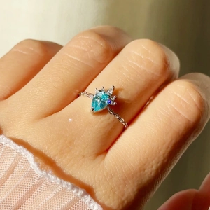 Close-up of blue teardrop gemstone ring with micro-pave diamonds and chain band