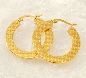 Close-up of gold hoop earrings with embossed star pattern on polished metal texture