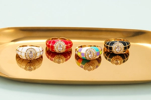 Golden enamel grid rings with colorful patterns and oval center stones on tray