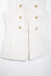 Detailed close-up of white tweed vest featuring gold buttons and woven texture