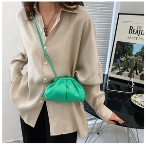 Detail of green pleated crossbody cloud bag worn by model in a stylish indoor setting