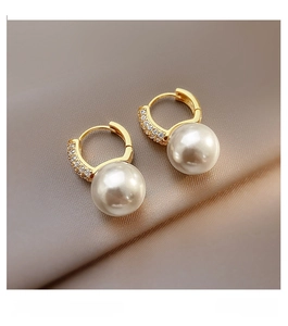 Detail shot of golden pearl hoop earrings with micro-set zircons on champagne satin background