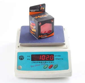 Weight measurement of 3x3 magic cube toy in black packaging box showing 102.0 grams