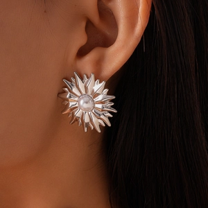 Detailed view of silver sunburst stud earring with white pearl on model's ear
