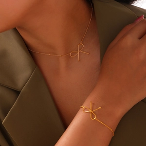 Minimalist gold bow-knot necklace and bracelet set worn by a model in a green blazer