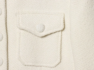 Dettaglio ravvicinato del tessuto tweed bianco crema con tasca a patta e bottone coordinato