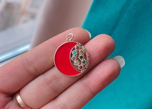 Handheld detail of a red enamel moon pendant with colorful zircon stones in gold finish