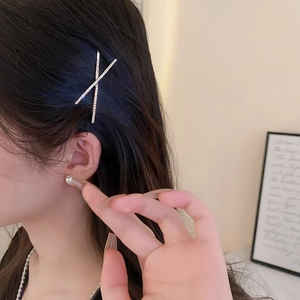 Close-up of a sparkling X-shaped hair clip with inlaid rhinestones on long black hair