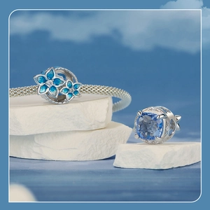 Detail of silver floral charm with blue enamel petals and faceted blue gemstone charm