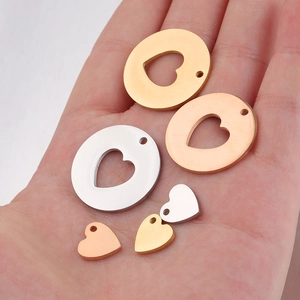 Detailed macro of stainless steel hollow and solid heart pendants held on a hand for scale