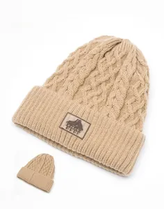 Dettaglio della maglia a trecce del berretto beige con patch logo in pelle pregiata