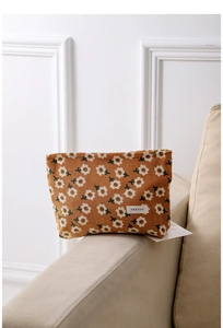 Close-up of floral corduroy makeup bag with H&R logo on a beige fabric sofa