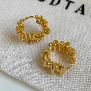 Irregular wrinkled gold hoop earrings with a textured lava finish on a white fabric bag