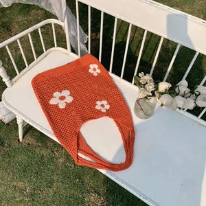 Detail der orangefarbenen Häkeltasche mit weißen Blumenmustern auf einer Gartenbank