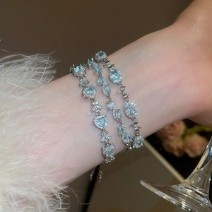 Close-up of aquamarine zircon bracelets with silver finish and bowknot details on a wrist
