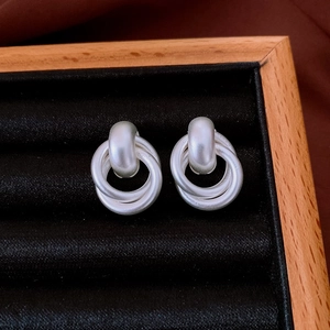Close-up of silver knot earrings on black velvet display within a wooden frame box
