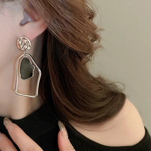 Détail de boucles d'oreilles géométriques dorées avec incrustations sombres sur mannequin