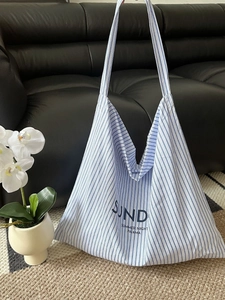Large blue and white striped canvas tote bag on a black leather sofa with a potted orchid