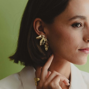 Close-up of model wearing 18K gold petal leaf earrings and irregular ring on green background