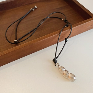 Détail du pendentif cosse de pois argenté sur cordon noir posé sur du bois