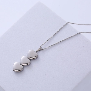 Elegant silver heart necklace with three polished pendants on a purple textured surface