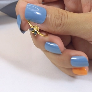 Detailed macro view of a gold bee ring with blue gemstone on model's finger