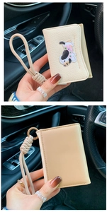 Detail of cream fabric card holder with cute dachshund embroidery and braided hand strap