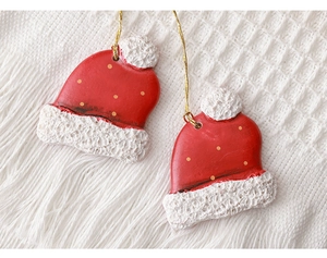 Detail view of miniature red Christmas hat ornaments with gold dots on white knit fabric