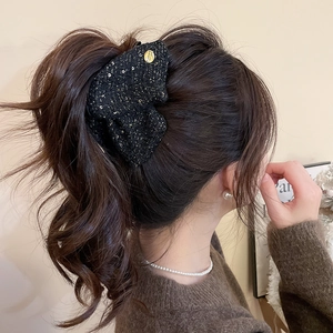 Detail view of tweed bow hair claw with gold threads on model's elegant ponytail hairstyle