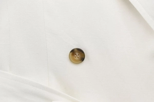 Detailed close-up of a brown tortoiseshell button on a white woven fabric dress
