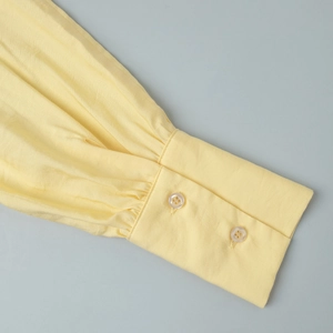 Detail of pale yellow lantern sleeve cuff with double buttons and fine gathering pleats