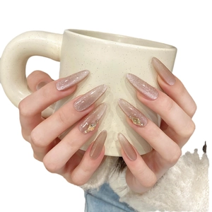 Pink cat eye almond press-on nails with golden rhinestones on a white ceramic mug