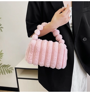 Detail of pink plush handbag with stripe design and decorative pom-pom handle on model