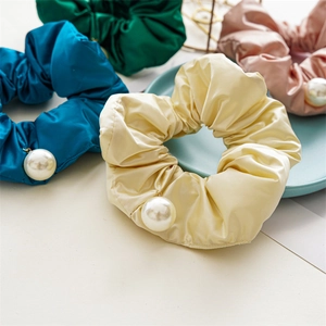 Detail of four satin hair scrunchies in green blue pink and beige with faux pearls