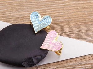 Close-up of pink and blue enamel heart rings on black stones with wood texture background