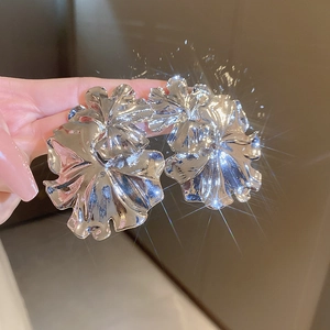 Macro shot of silver floral metal earrings with textured petals held in hand for scale