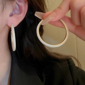 Macro detail of retro large gold hoop earrings with cream pearlescent resin texture