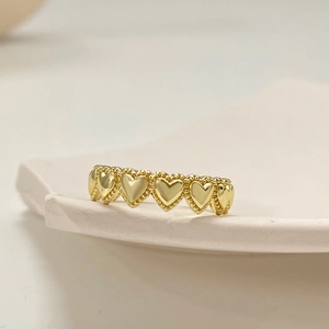 Dettaglio anello a cuori dorati con bordi perlati su una base di ceramica bianca