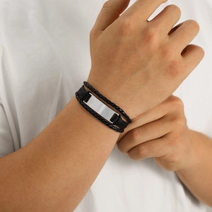 Detail of multi-layer woven black leather bracelet with silver metal plate on male wrist